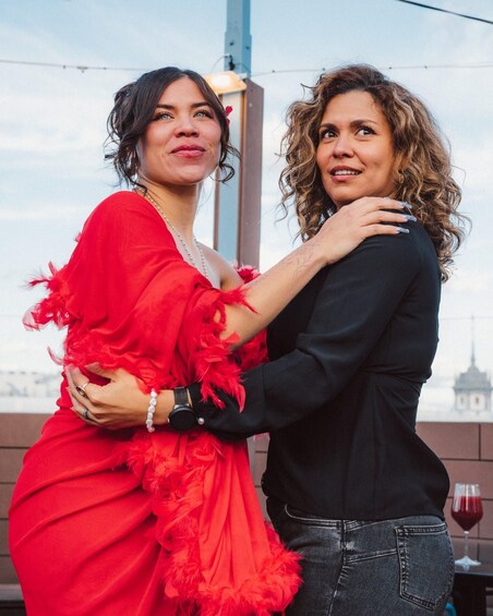 Two people embracing, one in a red dress and the other in black, with a cityscape in the background. 4