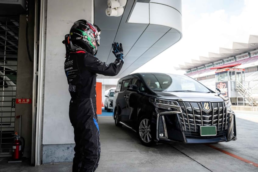 A person in a black and red racing suit standing next to a black car in a garage. 4