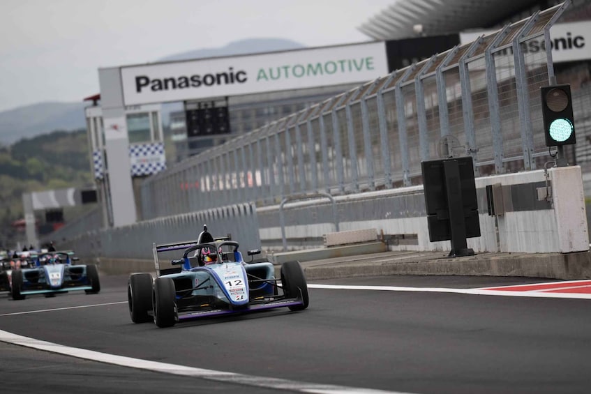 A race car on a track with a Panasonic Automotive sign in the background. 3