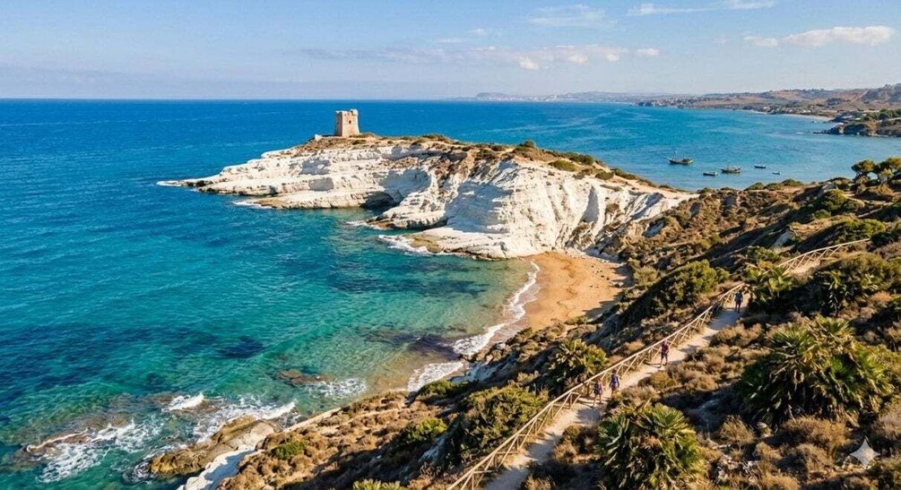 A coastal landscape with a rocky outcrop, clear blue sea, and a tower on the highest point. 2