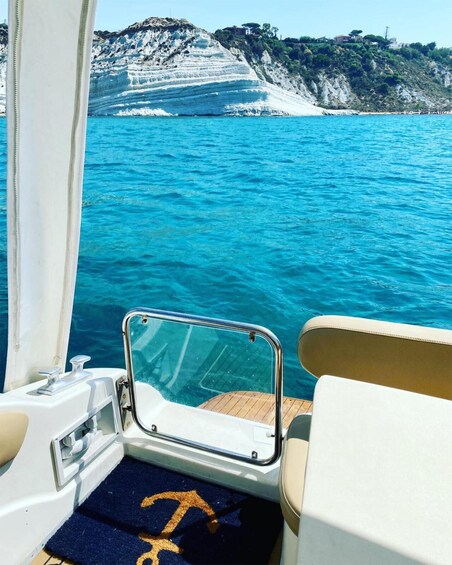 A boat's interior with a view of a coastal landscape featuring layered cliffs and a clear blue sea. 3