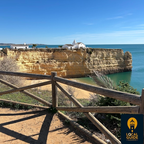 A coastal cliff with a white building, a wooden fence, and a clear blue sky. 1