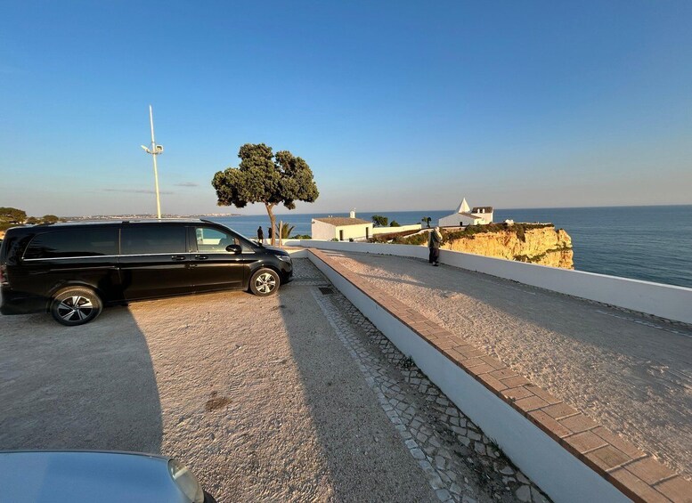 A black SUV parked on a coastal road with a clear view of the sea and a cliff in the background. 4