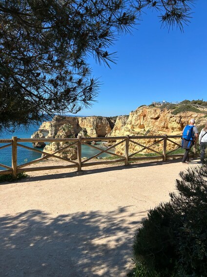 A coastal walkway with a wooden railing, clear blue sky, and rocky cliffs. 5