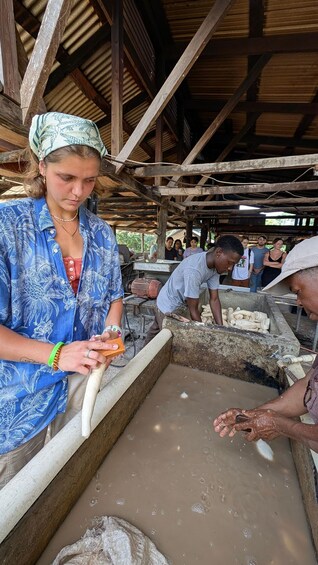A person holding a long, white object, possibly a tool, in a workshop with wooden beams and a water trough. 4