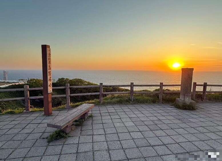A sunset over the ocean with a wooden fence and a bench. 5