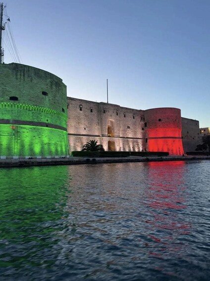 A historic fort with green and red illuminated sections, reflecting on the water. 4