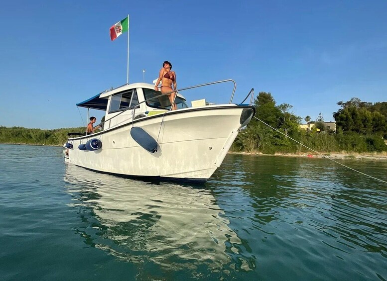 A boat with a flag, calm water, and greenery along the shore. 1