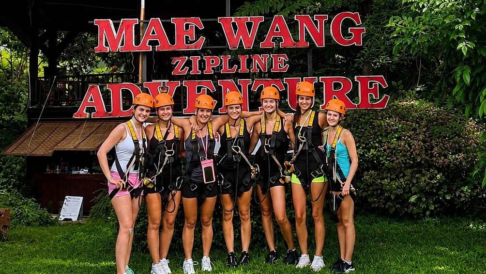 Un grupo de personas con cascos y arneses frente a un cartel que dice 'MAE WANG ZIPLINE ADVENTURE'. 5