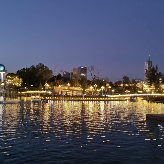 A river with reflections of lights, a bridge, and buildings in the background. 1
