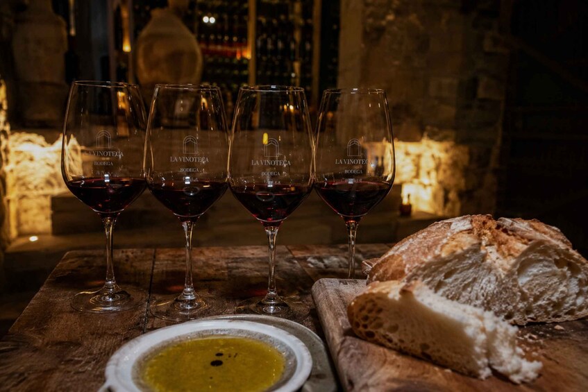 Four wine glasses with red wine, a bowl of olive oil, and a loaf of bread on a wooden table. 5