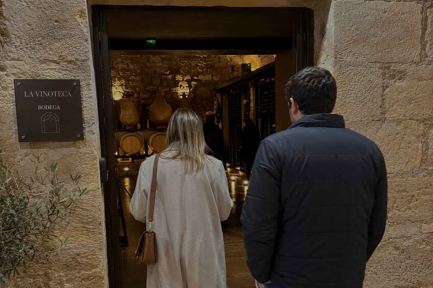A couple entering a wine cellar with a sign reading 'LA VINOTECIA BODEGA.' 3