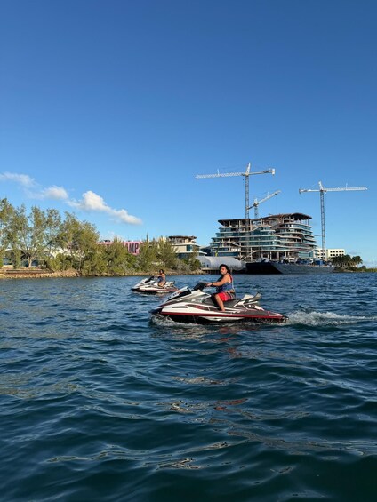 A person jet-skiing on a body of water with a large building and cranes in the background. 5