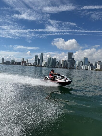 A person jet skiing on a body of water with a city skyline in the background. 1
