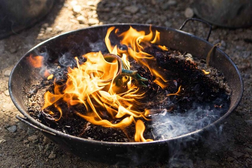 A metal pan with flames and embers on a rough surface. 1