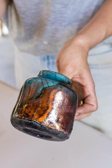 A hand holding a ceramic mug with a glossy finish and a teal lid. 4
