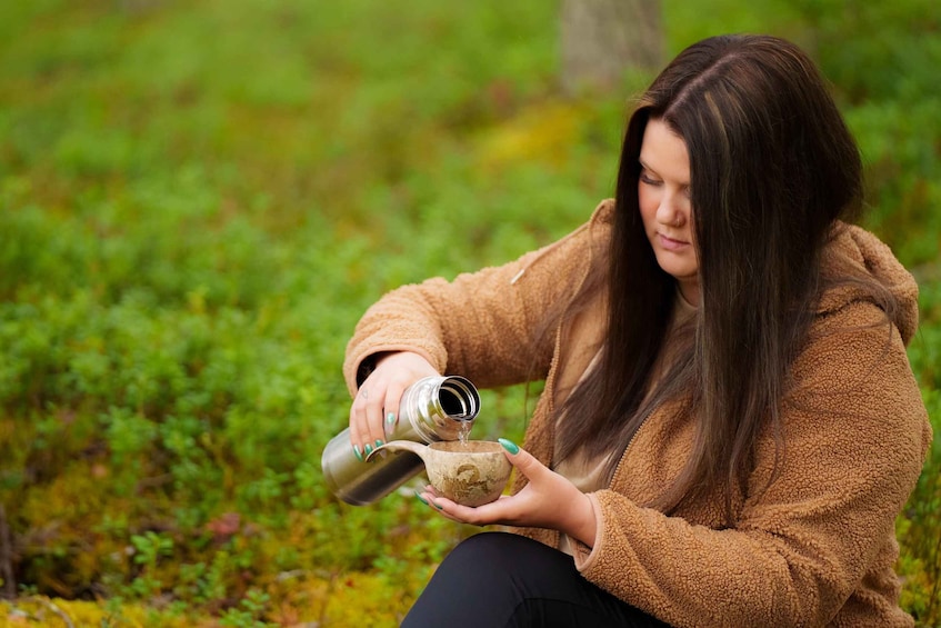 A person pouring liquid from a metal container into a ceramic mug. 2