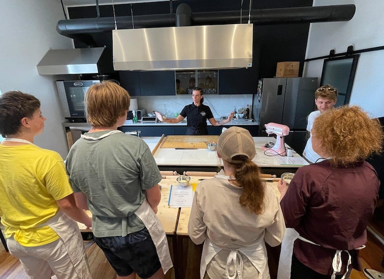 A group of people in a kitchen, some wearing aprons, with a chef demonstrating cooking techniques. 2