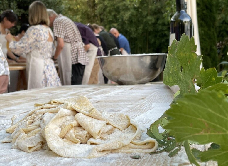 A group of people preparing food outdoors, with a table covered in flour and a large metal bowl. 1