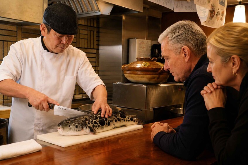 A chef preparing fish in a kitchen with stainless steel appliances and wooden bowls. 1