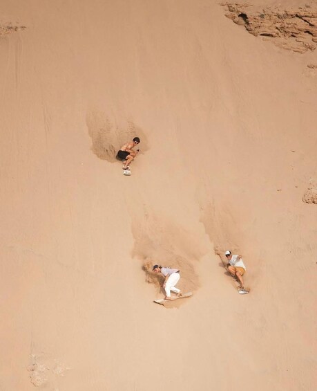 Two people sliding down a sandy slope. 1