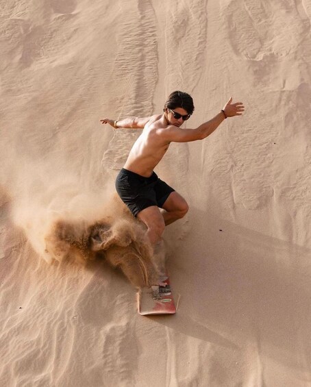 A person riding a sled on a sandy slope. 3
