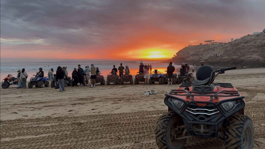 A sunset over a beach with people and ATVs. 2