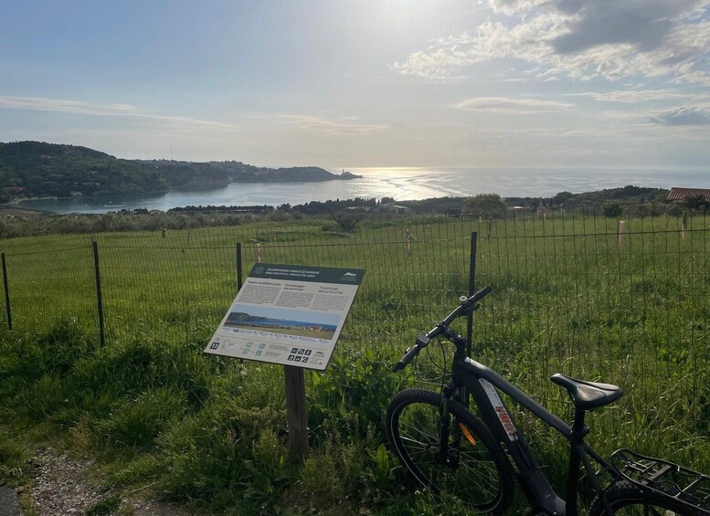 A mountain bike parked near a signboard in a grassy field with a view of a lake and hills in the background. 3