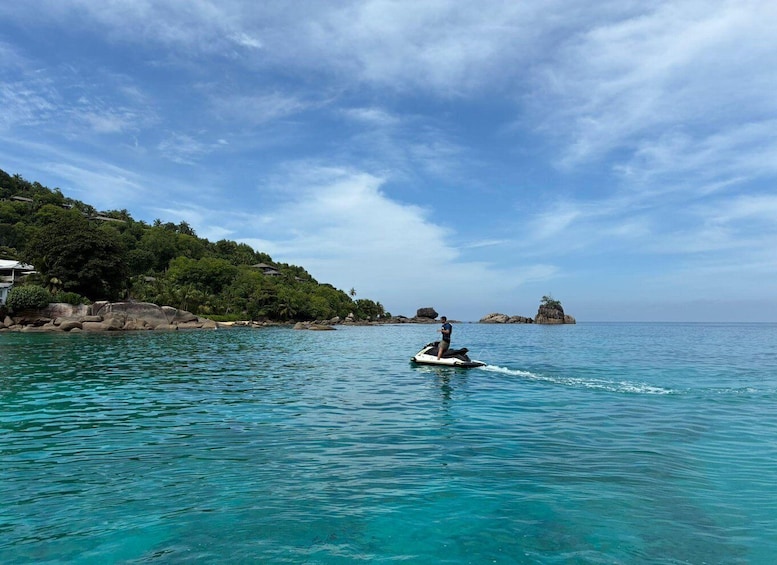 A person jet-skiing on clear turquoise waters with a coastal landscape and rocky outcrops in the background. 1