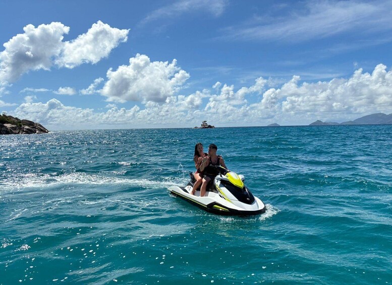 Two people jet-skiing on a clear blue sea with a rocky island in the background. 2