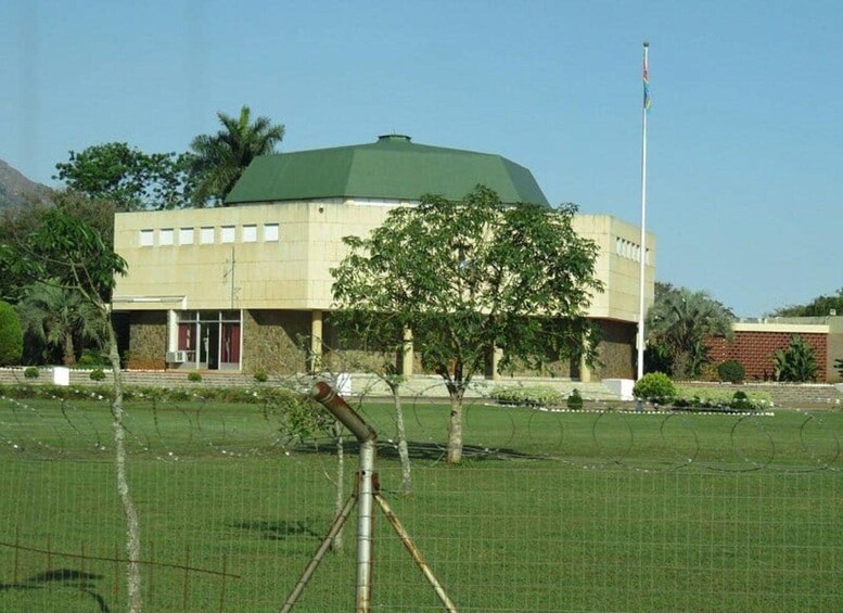 A building with a green roof, surrounded by a fenced area with trees and a flagpole. 1