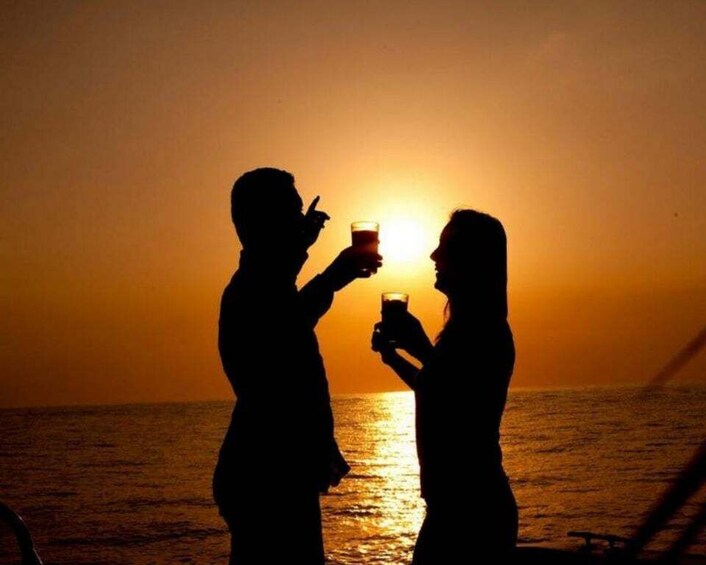 Silhouettes of two people holding drinks against a sunset over the ocean. 3