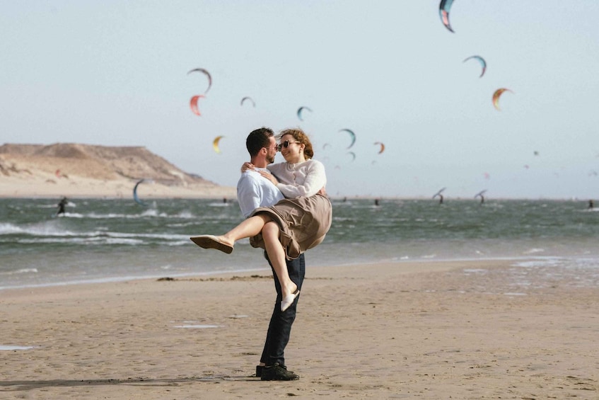 A couple on a beach with kites in the background. 1