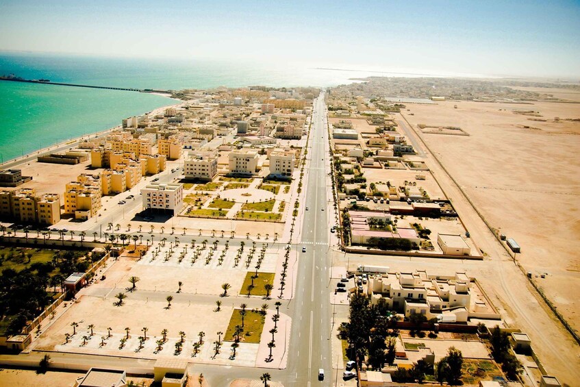 An aerial view of a coastal city with a long central road, buildings, and a beach. 2