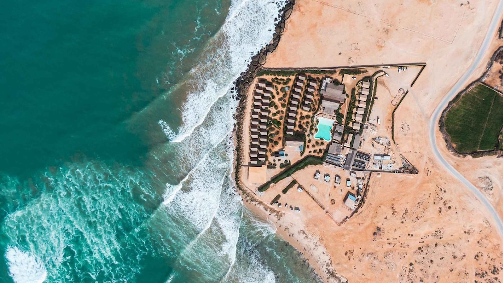 An aerial view of a coastal resort with a beach, a swimming pool, and several buildings. 4