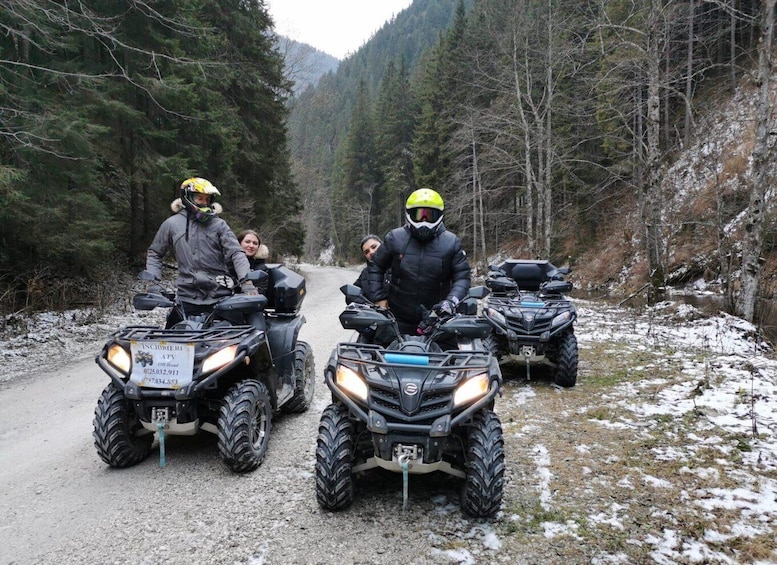 Three people on ATVs on a gravel road surrounded by forested mountains. 2