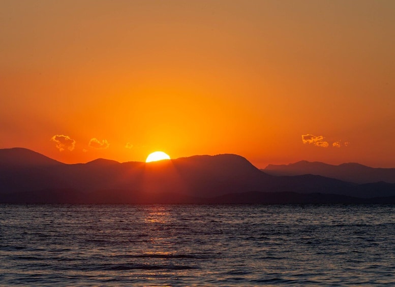 A sunset over a body of water with mountains in the background. 2