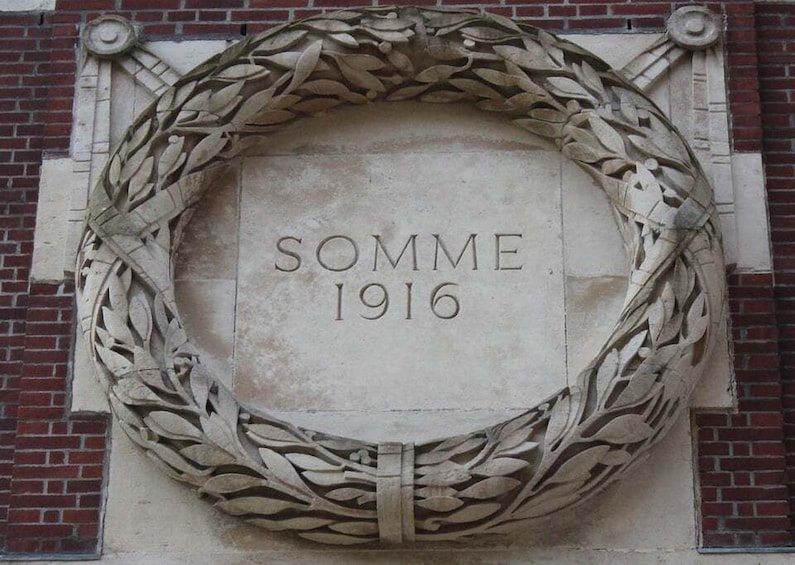 A stone plaque with 'SOMME 1916' inscribed, surrounded by a laurel wreath. 1
