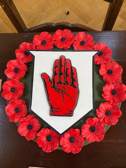 A table with a white shield-shaped placemat featuring a red handprint in the center, surrounded by red poppy flowers. 5