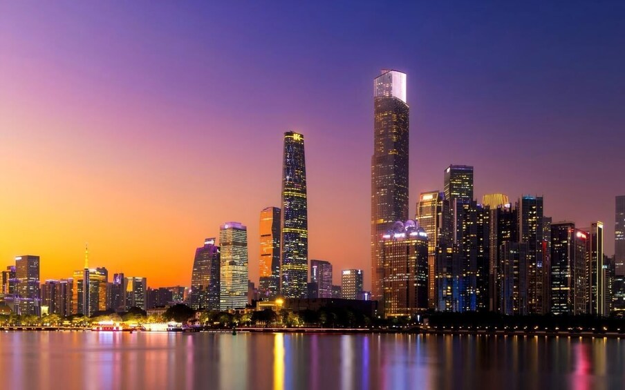 A city skyline at dusk with illuminated buildings reflecting on the water. 1
