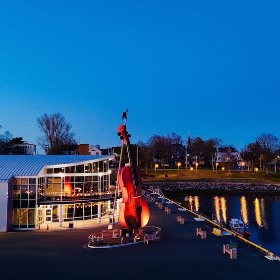 A large cello sculpture in front of a building with a glass facade. 1