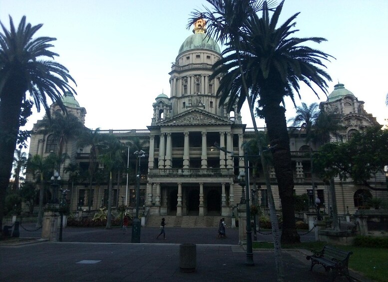 A grand neoclassical building with a large dome and columns, surrounded by palm trees and a paved plaza. 1