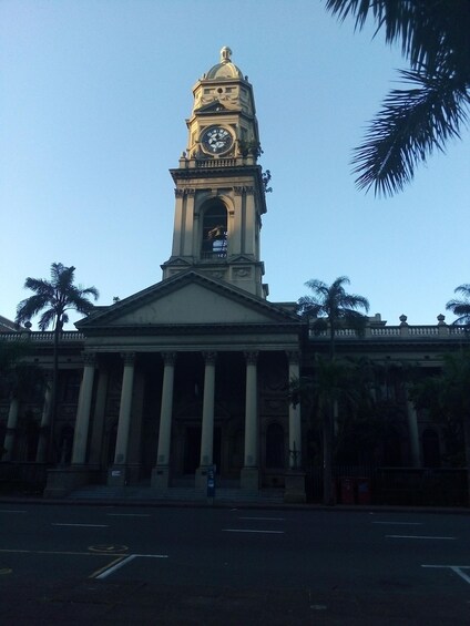 A grand building with a clock tower, palm trees, and a clear sky. 5
