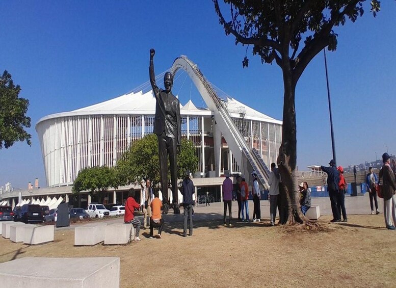 A statue of a man with raised arms, a large white building with a curved roof, and people gathered around. 4