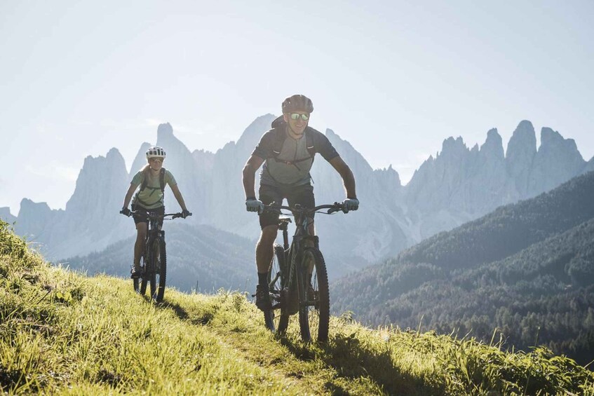 Two cyclists on a mountain trail with a mountainous landscape in the background. 1