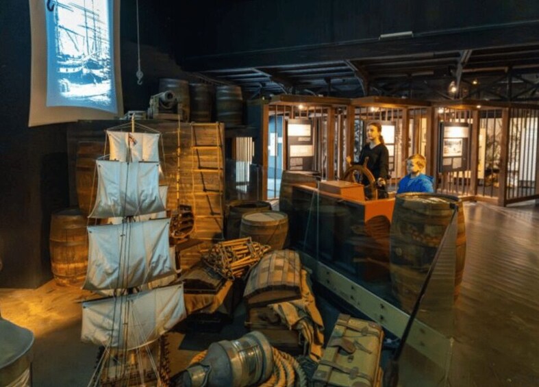 A maritime exhibit with ship models, barrels, and a person in a blue shirt. 1