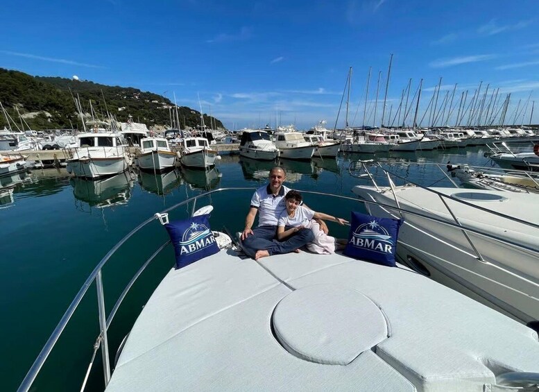 A marina with multiple sailboats docked, a person sitting on the deck, and a child beside them. 2