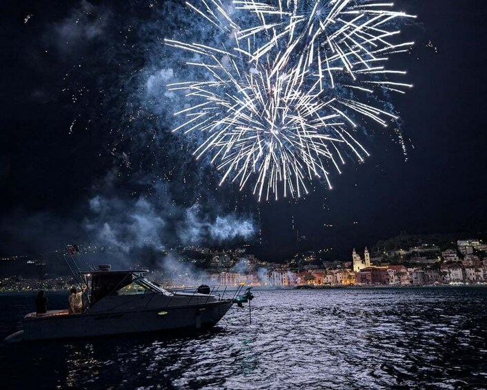 Fireworks over a body of water with a boat and a cityscape in the background. 1
