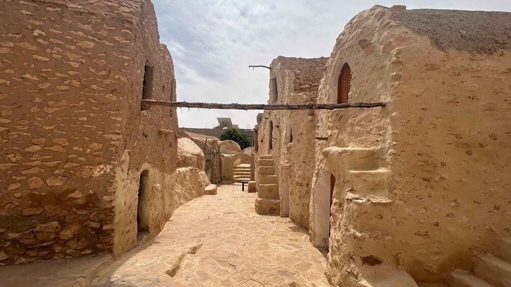 A narrow alleyway with stone buildings, arched doorways, and a wooden beam overhead. 4