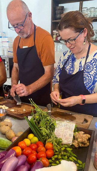 Two people in aprons preparing food with vegetables and spices on a counter. 5